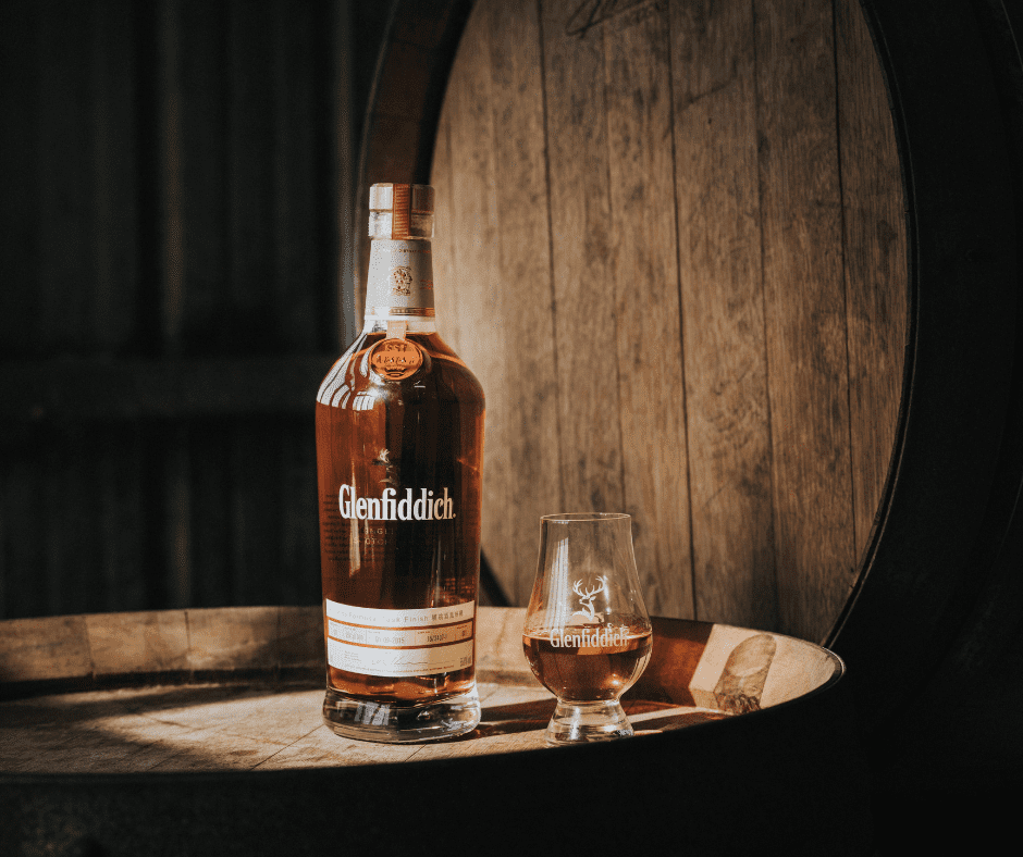 bottle of glenfiddich whisky on a barrel with a glass beside it