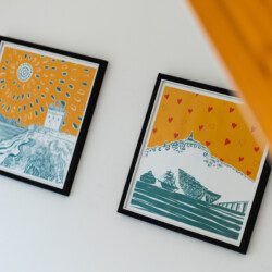Two blue and orange framed pictures hang on a white wall