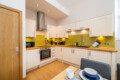 A bright kitchen with green wall, units with over counter units, oven, hob, microwave, kettle, toasted and sink